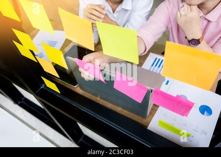Uomo d'affari di incollaggio note adesive sulla parete di vetro in ufficio e discussting con il team. Foto Stock