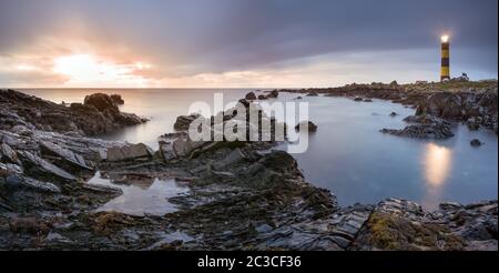 Twilight inizia a cedere alla luce del giorno al faro di St. Johns Point. Costa rocciosa con acqua e cielo sfocati, fotografia a lunga esposizione Foto Stock