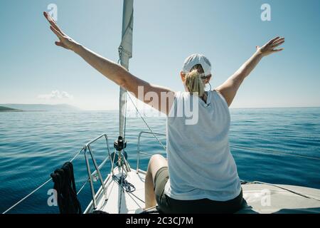 Donna seduta sulle navi prua godendo il viaggio yacht con le braccia aperte. Vela, vela e tr Foto Stock