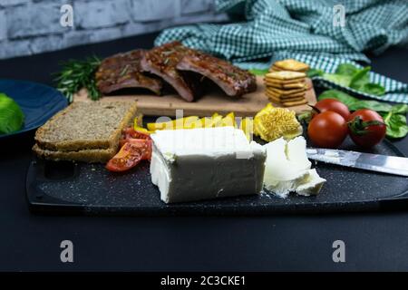 Costolette sotto salsa al miele su una tavola di legno accanto ai pomodori, peperoni e basilico con rosmarino, feta affettata con cracker. Viste dall'alto Foto Stock