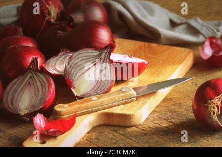 Cipolle rosse su tagliere di legno su sfondo di legno scuro a struttura rustica. Vista dall'alto, spazio per il testo . Foto Stock