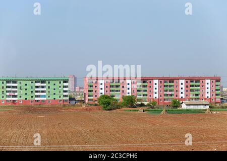 Kaesong, Corea del Nord - 5 maggio 2019: Quartiere residenziale con un tipico edificio di appartamenti e campi agricoli in primo piano Foto Stock