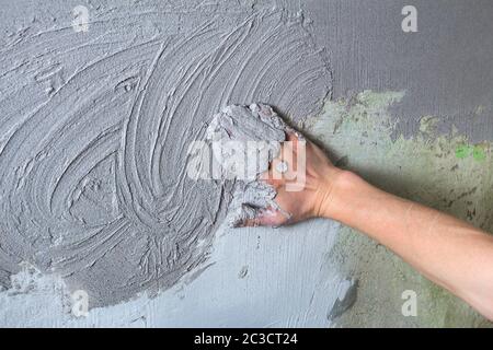 Il costruttore di intonaci mette il gesso sulla parete con la mano. Costruzione interna e lavori di finitura. La mano tiene il mix di costruzione e mq Foto Stock