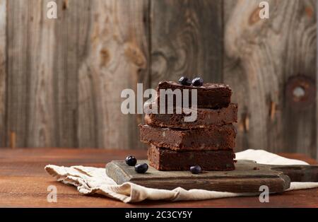 Pila di cotto quadrato fette di brownie torta al cioccolato con noci su una superficie di legno. Cuocere cibi fatti in casa. Pasticceria al cioccolato. Farina dolce casereccio Foto Stock