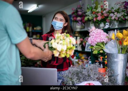 Asian Donna indossare maschera o maschera protettiva contro la crisi del coronavirus, Florist proprietario di un piccolo fioraio affari che tiene fiori per la consegna t Foto Stock