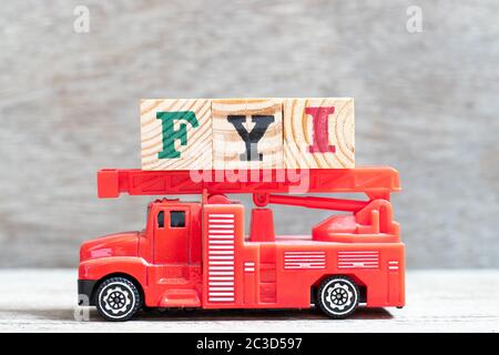 Il camion rosso del fuoco tiene il blocco della lettera in parola FYI (abbreviazione di per le vostre informazioni) su sfondo di legno Foto Stock