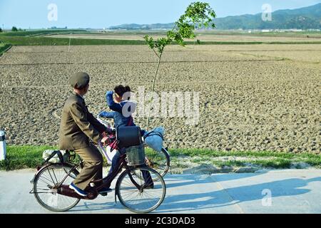 Regione di Wonsan, Corea del Nord - 3 maggio 2019: Una gente del posto che guida una bicicletta lungo la strada di campagna. Сountryside, vicino al porto di Wonsan. Uomo e donna Foto Stock