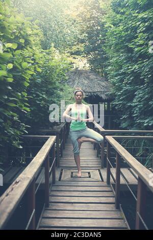 Donna meditante su ponte di legno in foresta Foto Stock