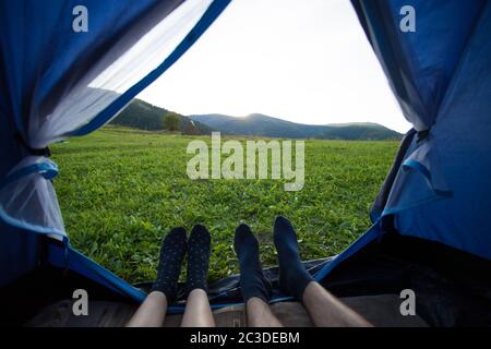 Due persone che si stendano in tenda, vista dall'interno. Campeggio coppia con splendida vista sulle montagne tramonto Foto Stock