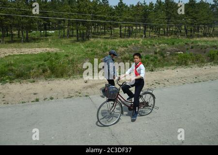 Corea del Nord - 4 maggio 2019: Un ragazzo, membro della Pioneer Youth Union, sta andando a casa in bicicletta dopo la scuola. Сountryside, vicino al porto di Wonsan. Vecchio Foto Stock