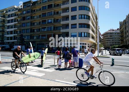 Ciclisti sulla strada del quartiere di Gros con surfisti che trasportano surf da tavola e turisti che trasportano i luggages.San Sebastian.Basque Country.Spain Foto Stock