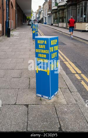 Ramsgate, UK - Giugno 19 2020 UN cartello di promemoria di allontanamento sociale più una richiesta di tenere la sinistra sulla strada con doppie linee gialle. Un uomo locale sta camminando Foto Stock