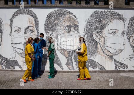 Un team di professionisti della salute parla, mentre si trova accanto ai graffiti durante l'inaugurazione dell'artista.artista portoghese, Alexandre Faro noto come Whils incise set di ritratti su un muro all'ospedale di Sao Joao in onore dei professionisti della salute per la lotta contro la covid 19 pandemia. Foto Stock