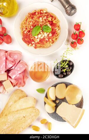 Cucina italiana. Pasta, formaggio, prosciutto, vino, pomodori, farciti dall'alto su fondo bianco Foto Stock