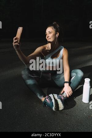 Giovane runner femminile che posa in abbigliamento sportivo prendendo selfie con il suo cellulare. Ragazza che si gode un pomeriggio di esercizio in estate e di scattare foto. Foto Stock