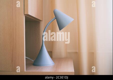 Particolare di camera da letto accogliente - lampada da lettura su comodino in legno. Tenda unicolor sullo sfondo. Design semplice e moderno Foto Stock