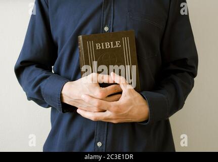 L'uomo, sacerdote o credente, sta tenendo la Bibbia Santa, libro religioso del cristianesimo, con le mani aggrappate. Metafora della preghiera o della predicazione Foto Stock