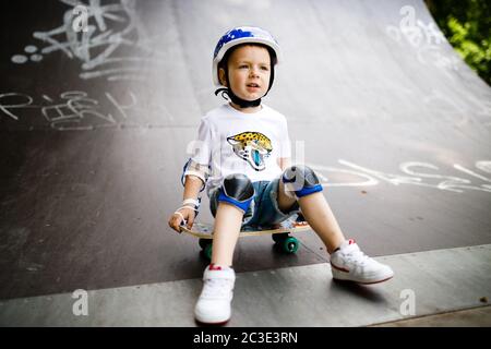 Ragazzo con un skate in un parco di skate. Il ragazzo impara a pattinare, in piena protezione. Foto Stock