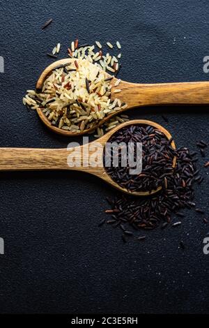 Riso biologico nero e selvatico in cucchiai di legno come ingredienti da cucina su fondo di cemento con spazio di copia Foto Stock