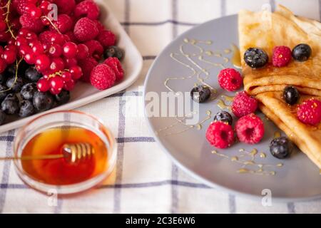 Due frittelle ripiegate in casa con miele e lamponi freschi maturi e more su piatto di porcellana grigia su tavolo da cucina Foto Stock