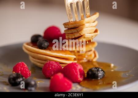 Tagliate parte del gustoso pancake fatto in casa sul piatto con miele fresco, lamponi e more durante la colazione Foto Stock