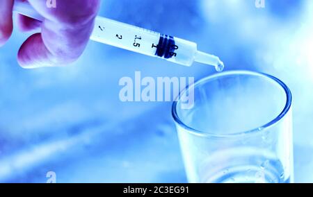 un ricercatore svuota il liquido da una fiala in un contenitore di vetro per trovare un vaccino anti virus in una scie Foto Stock