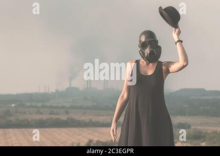 Giovane ragazza in un vestito nero e maschera a gas sullo sfondo di fumo fabbrica camini in Ucraina primo piano Foto Stock