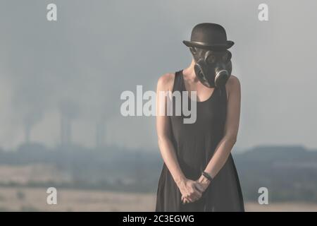 Giovane ragazza in un vestito nero e maschera a gas sullo sfondo di fumo fabbrica camini in Ucraina primo piano Foto Stock