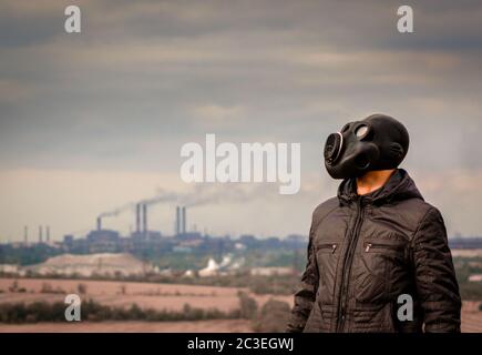 uomo in una maschera a gas in mezzo al fumo da tubi di fabbrica Foto Stock