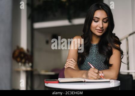 Studente indiano che studia in biblioteca, impara la lingua, prende appunti, prepara gli esami. Ritratto di bella donna asiatica freelance sul posto di lavoro Foto Stock