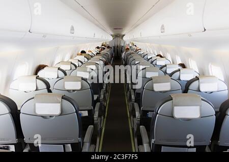 Lunga corsia con file di posti a sedere e passeggeri in cabina di un aereo (salone) Foto Stock