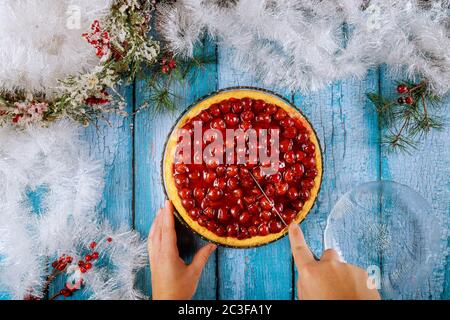 Le mani femminili stanno tagliando la torta di ciliegia su un tavolo di legno blu con decorazione di cristmas. Foto Stock