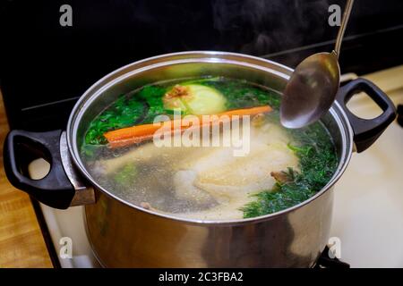 Preparare il brodo di pollo con le verdure in una pentola di acciaio con cucchiaio. Foto Stock