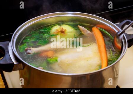 Brodo di pollo caldo con carote, pollo intero, cipolla, sedano e prezzemolo in pentola d'acciaio. Foto Stock