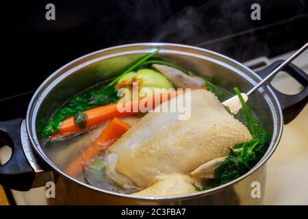 Brodo di pollo bollente con verdure sane in pentola di acciaio su piano cottura a gas. Foto Stock