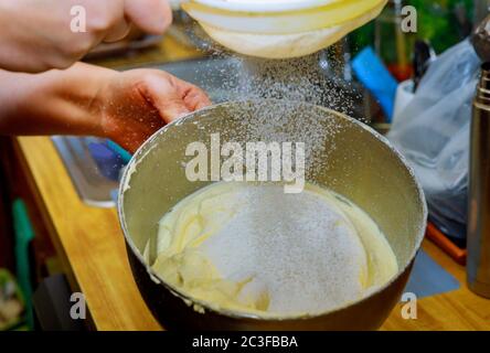 La donna setola la farina nel recipiente del mixer con il composto di uova. Preparazione dell'impasto per torte. Foto Stock