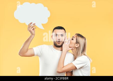 Giovane donna sussurrando segreti all'uomo con la bolla di pensiero carta Foto Stock