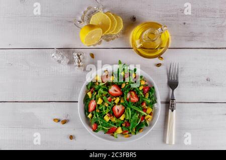 Insalata verde con rucola, fragole e mango con olio d'oliva, limone e forchetta. Foto Stock