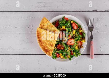 Insalata con rucola, ananas, pistacchi e fragole su un piatto bianco con pita pane. Foto Stock