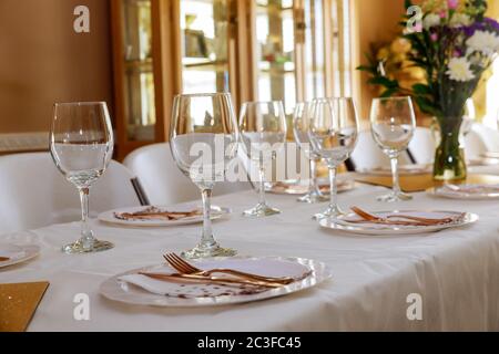 Tavolo festivo servito per cena o festa con bicchieri e fiori in soggiorno. Foto Stock