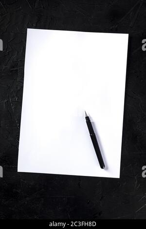 Un foglio bianco di carta A4 con una penna a inchiostro, girato dall'alto su uno sfondo nero, un mockup Foto Stock