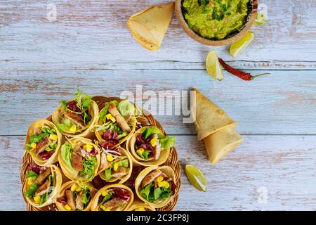 Coni di tortilla ripieni con fajita su cesto di vimini con calce e guacamole su tavolo di legno. Foto Stock