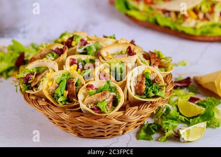 Tortillas cono farcito con verdure e carne su cesto con insalata verde su tavola bianca. Cucina messicana. Foto Stock