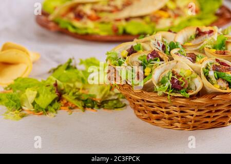 Tortillas cono farcito con verdure e carne su cesto con insalata verde su tavola bianca. Cucina messicana. Foto Stock