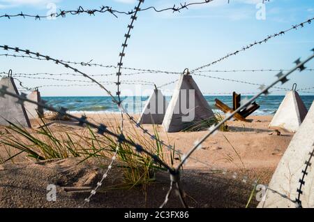 Filo spinato e recinto militare in cemento sulla spiaggia vicino al mare in Crimea Foto Stock