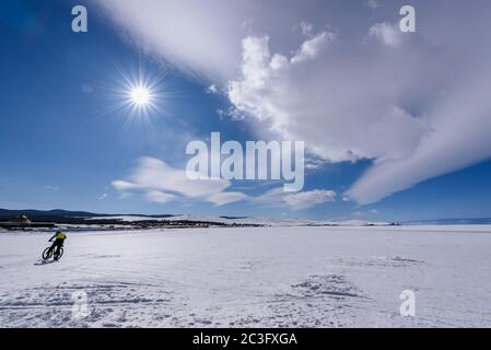 Silhouette di uomo corre in bicicletta sul lago ghiacciato Baikal in tempo soleggiato con belle nuvole cielo Foto Stock