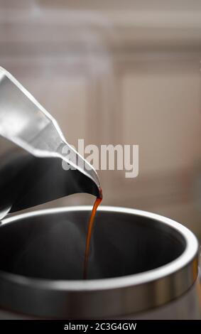 Versare il caffè dalla tazza di moka in una grande tazza termica metallica con flusso che si alza. Mattina con espresso. Foto Stock