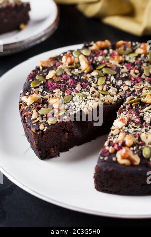 Torta di cioccolato alla barbabietola e alla cotta con pecan, semi di zucca su un piatto bianco posto su sfondo nero Foto Stock