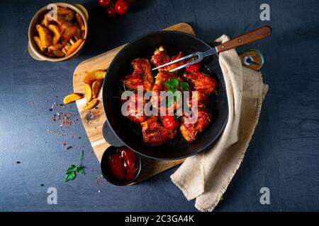 Ali di pollo speziate al miele con spicchi di patate Foto Stock