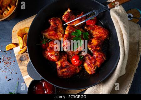 Ali di pollo speziate al miele con spicchi di patate Foto Stock